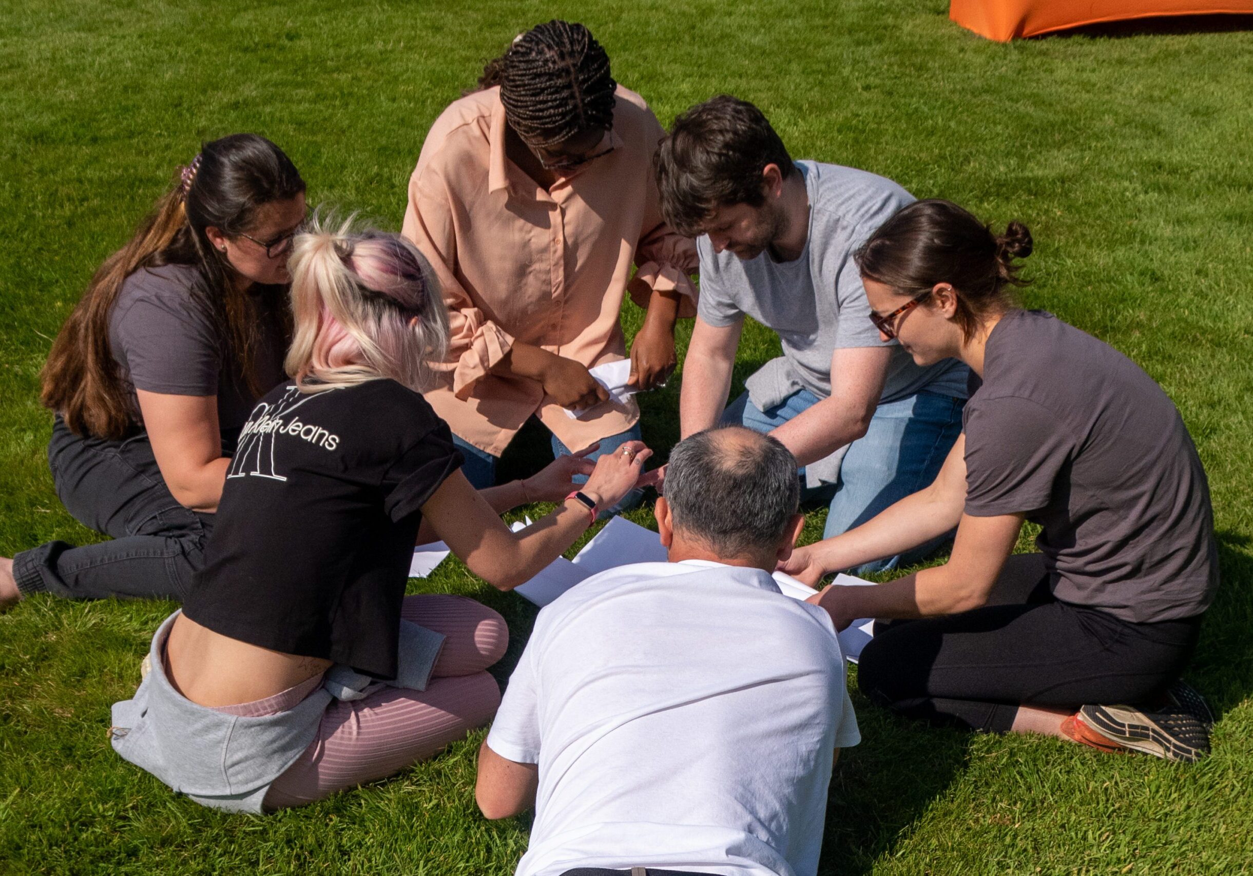 A team of Hyphen8 staff are sat on the grass on a sunny day doing a team building exercise.