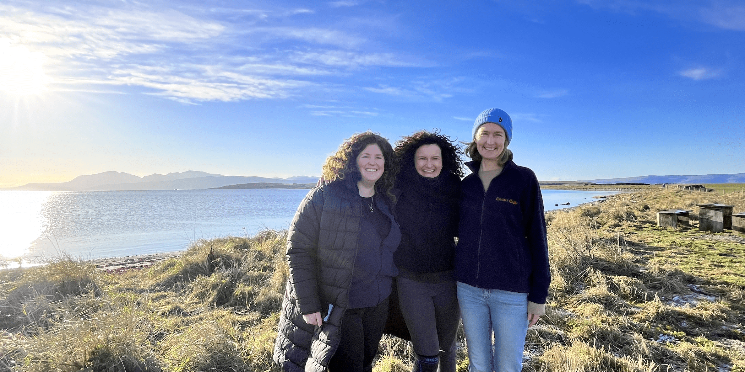 Three women stand together smiling, on a crisp wintery day.